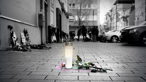 Eine Kerze steht auf der Straße, daneben liegt eine Rose