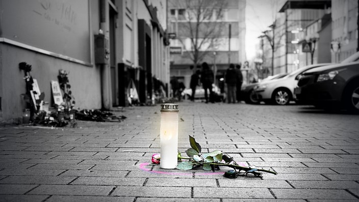 Eine Kerze steht auf der Straße, daneben liegt eine Rose 