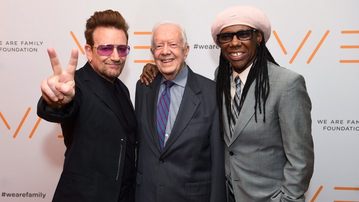 Jimmy Carter steht zwischenden Musikern Bono und Nile Rodgers