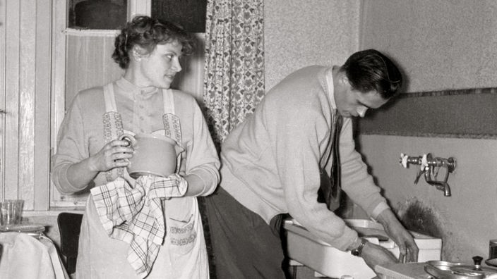 Frau und Mann befinden sich gemeinsam in der Küche und erledigen die Hausarbeit.