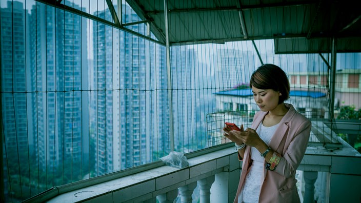 Asiatische Frau auf einem Balkon, schaut auf ihr Smartphone