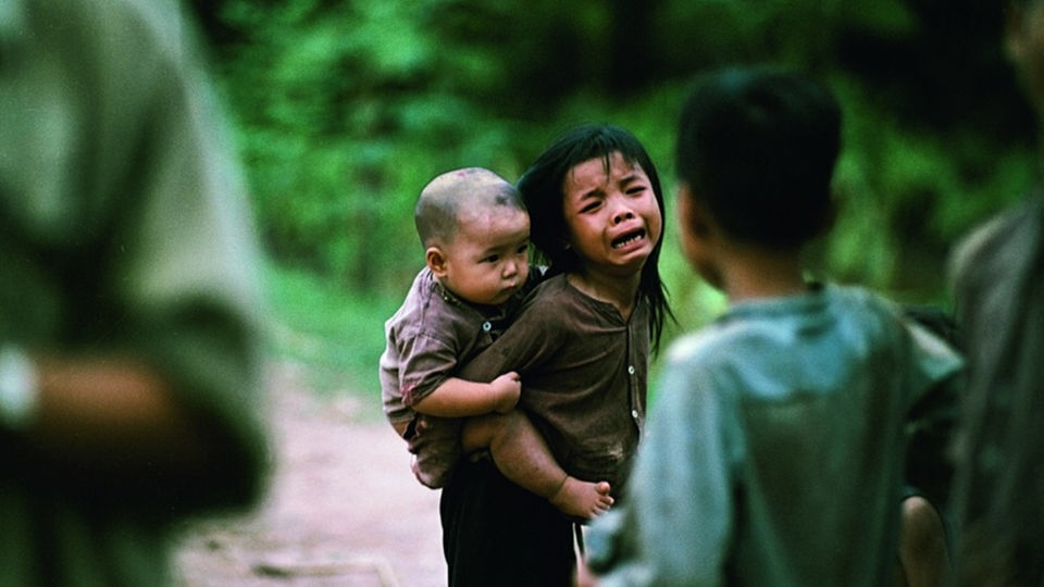 Ein junges Mädchen weint verzweifelt und trägt auf ihrem Rücken ein Baby.
