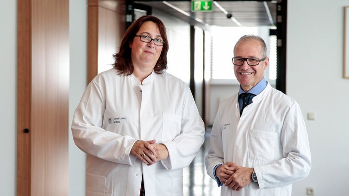 Die Kölner Rechtsmedizinerin Frau Dr. Banaschak und Prof. Dr. Markus Rotschild stehen in einem Flur und lächeln in die Kamera