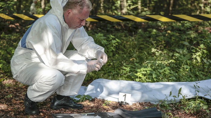 Eine Leiche am Tatort nahe am Waldparkplatz wird von einem Mitarbeiter der Spurensicherung untersucht. (Szene nachgestellt)