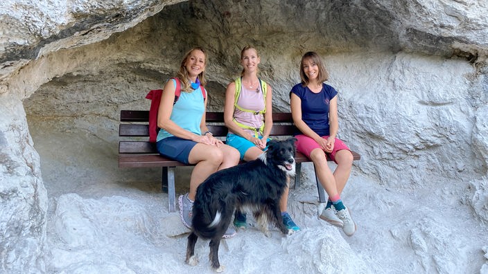 Tamina Kallert (l), Helena Plath (m) und Silvia Mai sitzen auf einer Bank unter einem Felsüberhang