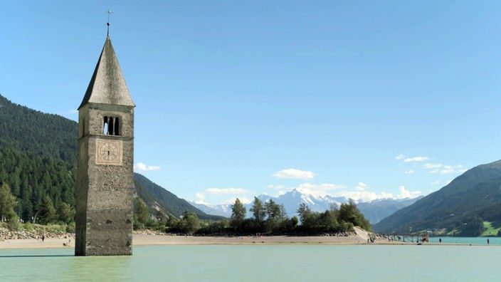Einfacher quadratischer Kirchturm aus Bruchsteinen ragt aus einem See