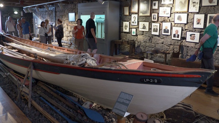 Besucher in einem Ausstellungsraum im Museum in Lajes mit einem Walfängerboot