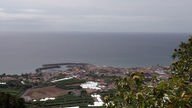 Blick von einem Berg auf die Küste der Insel Sao Miguel mit Hafenort und Atlantik