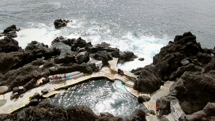 Blick von oben auf die felsige Küste mit einem natürlichen Pool mit betonierter Umrandung