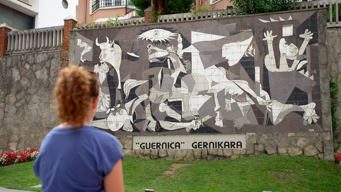 Anne Willmes steht vor einer Wand mit der Abbildung des Gemäldes Guernica