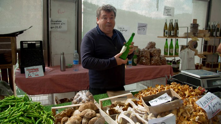 Marktverkäufer an einem Stand mit Pilzen hält eine Flasche Wein hoch