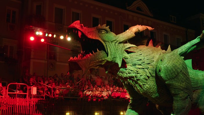 Große, angeleuchtete Drachenfigur, im Hintergrund Publikum auf einer Tribüne