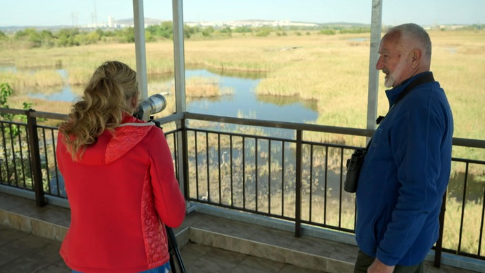 Tamina Kallert und ein Mann stehen auf einer Aussichtsplattform und schauen auf ein Naturschutzgebiet