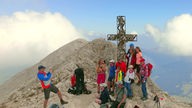 Jemand macht ein Foto der Gruppe am Gipfelkreuz des Plattkofel