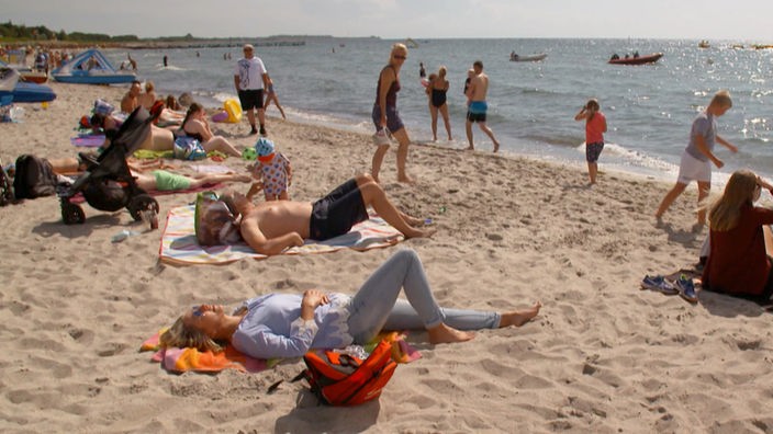 Andrea Grießmann sowie weitere Badegäste liegen oder laufen an einem Sandstrand