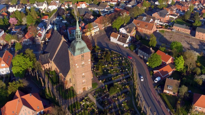Luftaufnahme eines Ortes mit Backsteinkirche und kleineren Häusern