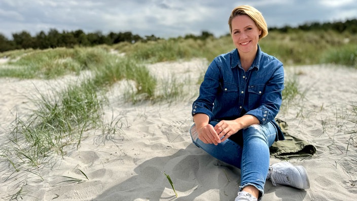 Judith Rakers sitzt im Sand am Strand