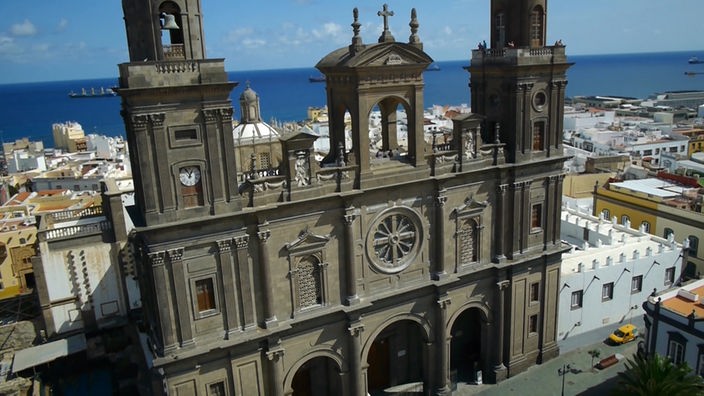 Prächtige Kirchenfassade mit zwei Türmen, dahinter Stadthäuser und das Meer