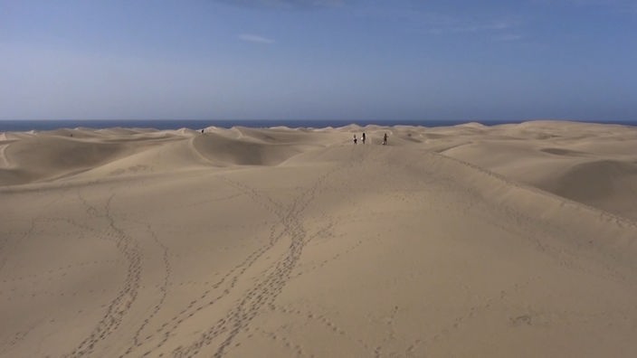 Drei Personen auf einer riesigen hügeligen Sandfläche