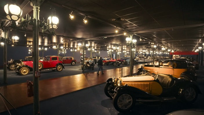Blick in riesige, mit historischen Laternen beleuchtete Ausstellungshalle voller Oldtimer