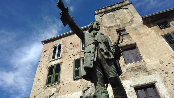 Statue eines Freiheitskämpfers vor Hausfassade mit Einschusslöchern