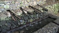 Die Quellen von Epina: Aus hölzernen Rohren plätschert Wasser in einen Steintrog