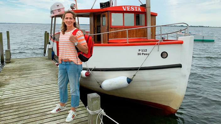 Tamina Kallert steht mit rotem Rucksack auf dem Landungssteg vor dem Postboot