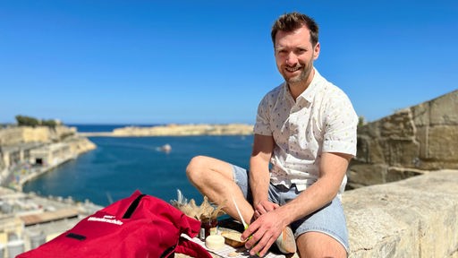 Daniel Aßmann bei einem kleinen Picknick mit maltesischen Spezialitäten und Blick auf den Hafen von Valletta.