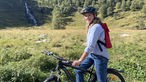 Tamina Kallert sitzt auf einem Fahrrad inmitten einer Wiesen-Wald-Landschaft