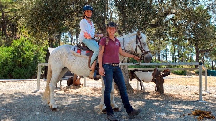 Tamina Kallert (l) sitzt auf einem weißen Pferd, das von Elpida Hatziioannou-Idé am Zügel gehalten wird