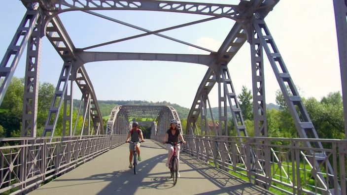 Daniel Aßmann auf dem Fahrrad sowie eine Radfahrerin überqueren eine Stahlbrücke