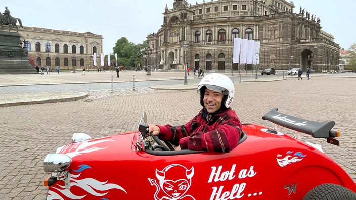 Ramon Babazadeh sitzt in einem kleinen roten Fahrzeug, im Hintergrund die Semperoper
