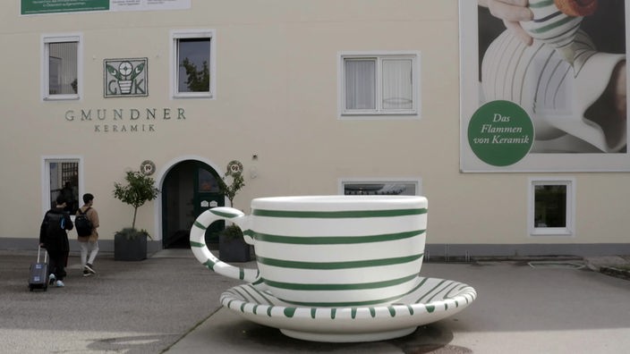 Überdimensional große Tasse mit grünen Querstreifen und Untertasse stehen vor einem Haus