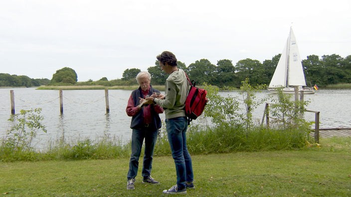 Wilfried Erdmann und Jo Hiller stehen auf einer Wiese am Ufer der Schlei