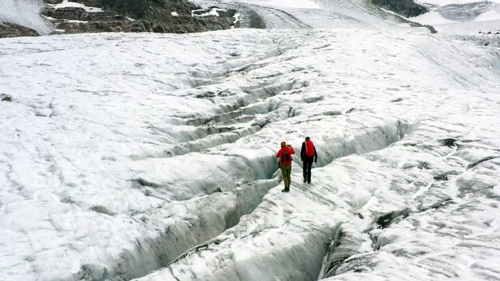 Zwei Personen stehen auf einem Gletscher vor einer tiefen Spalte