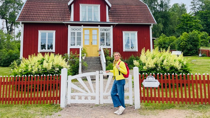 Tamina Kallert steht an einem Zaun vor einem roten Holzhaus