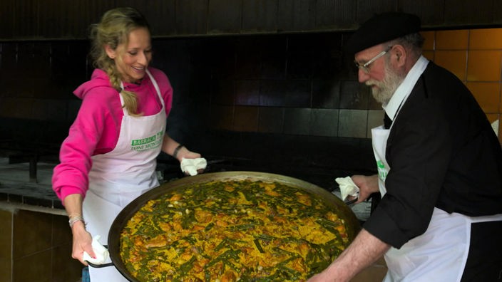 Tamian Kallert hilft dem Koch Toni Montoliu beim Tragen der gefüllten Paellapfanne