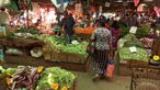 Mehrere Personen zwischen Marktständen mit frischem Gemüse