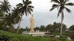 Hohe, weiße Buddhastatue auf einem von Wasser umgebenen Podest, darum herum mehrere Palmen