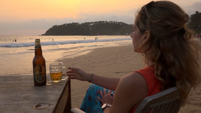 Tamina Kallert sitzt mit einem Bier am Strand und schaut aufs Meer
