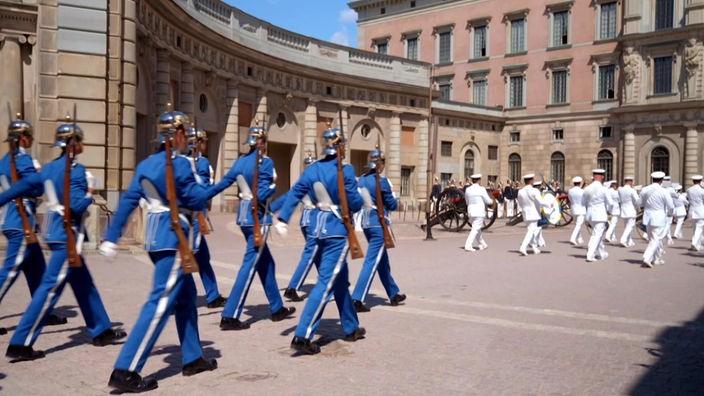 Wachsoldaten in blauen Uniformen und mit Gewehren marschieren im Schlosshof