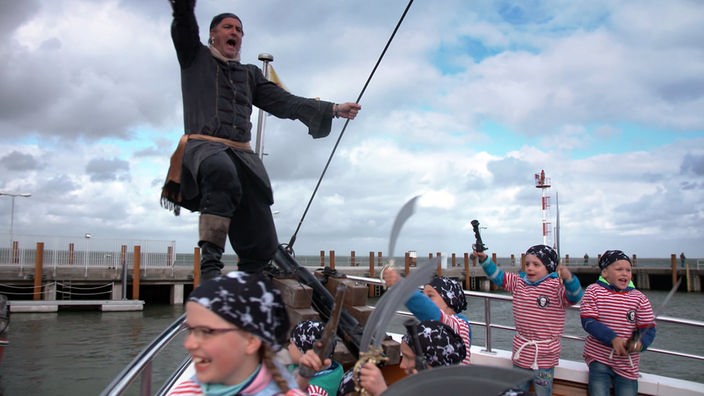 Kleine Kinder in Piraten-Look und mit Säbeln ausgestattet an Bord eines Schiffes