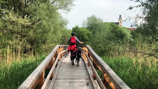 Tamina Kallert schiebt ihr Fahrrad über eine schmale Holzbrücke