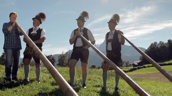 Stefan Pinnow bläst das Alphorn neben drei traditionell gekleideten Alphornbläsern