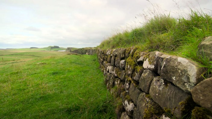 Langer Wall aus Bruchsteinen zieht sich durch eine Wiesenlandschaft
