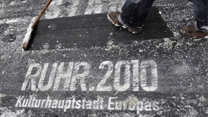 Verschneiter schwarzer Teppich mit Schriftzug Ruhr 2010 Kulturhauptstadt Europas, Fuß Schneeschieber