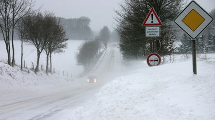 Ein Auto fährt durch eine schneeverwehte Straße