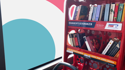 In einem Linienbus steht hinter dem Fahrersitz ein Regal mit Büchern