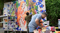 Zwei Männer arbeiten an einem Wandgemälde.