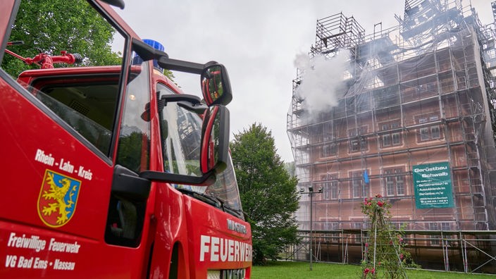 Aus einem eingerüsteten Gebäude kommt Rauch, davor steht ein Feuerwehr-Wagen.
